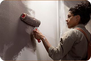 A painter applying gray paint to a smooth wall surface using a roller brush.